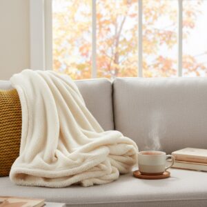 Kuschelige elektrische Heizdecke aus Fleece auf einem hellen Sofa neben einer dampfenden Tasse Tee